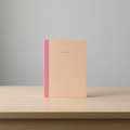 Cuaderno de notas tapa crema con lomo rosa sobre escritorio